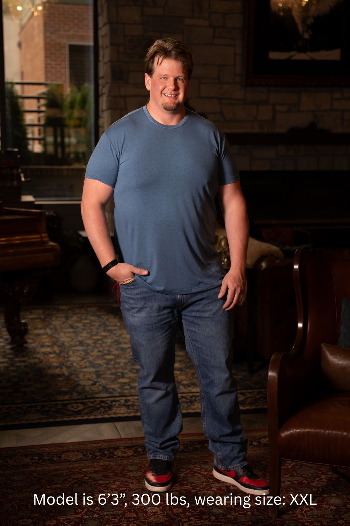 6'3", 300 pound man wearing a blue XXL t-shirt and jeans standing in a room with wooden furniture.