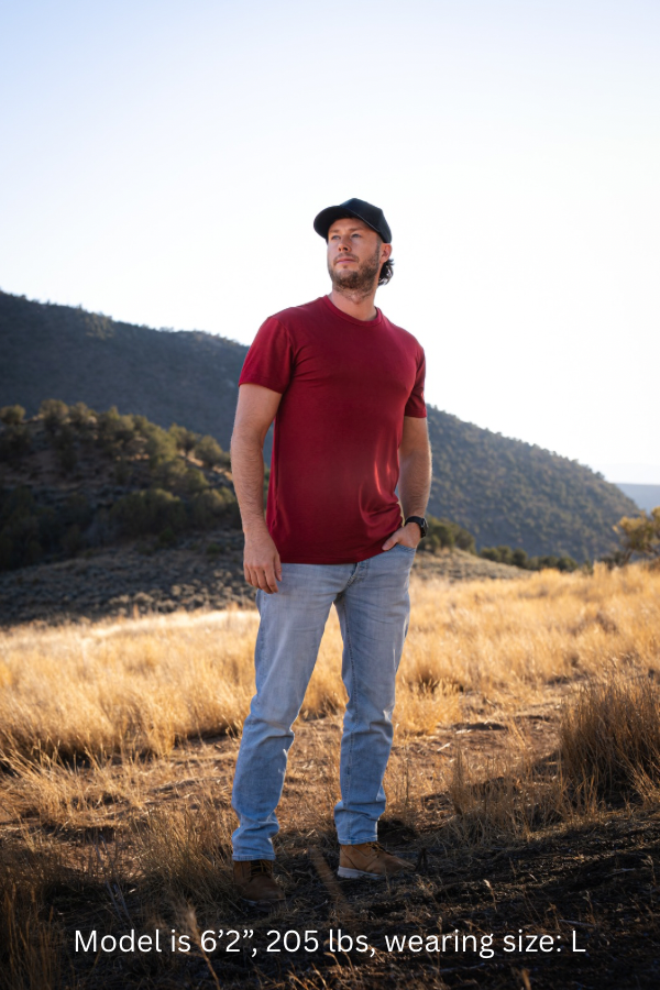 6'2" - 205# Man wearing a red t-shirt and blue jeans standing in a field with mountains in the background
