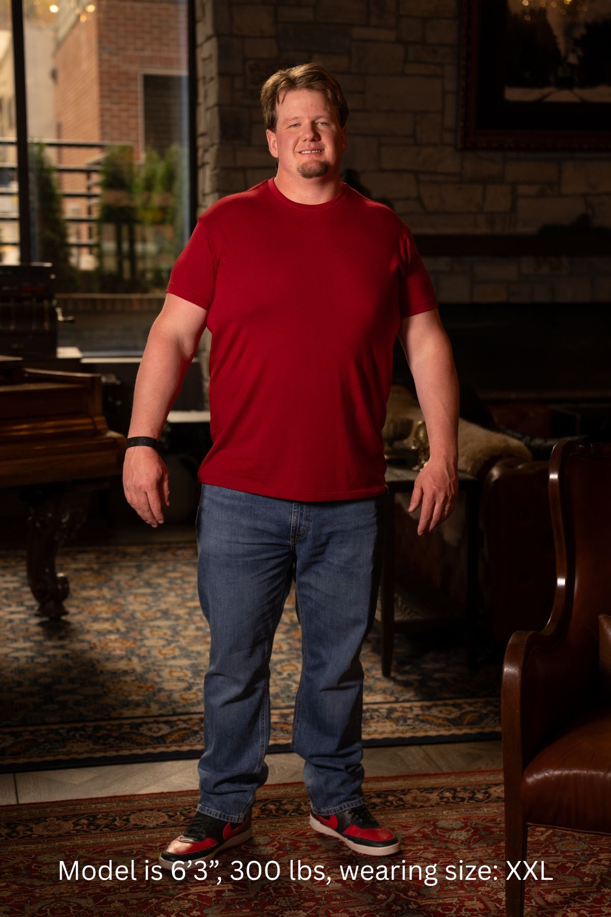 6'3", 300 pound man wearing a red XXL shirt and blue jeans standing in a room with furniture.