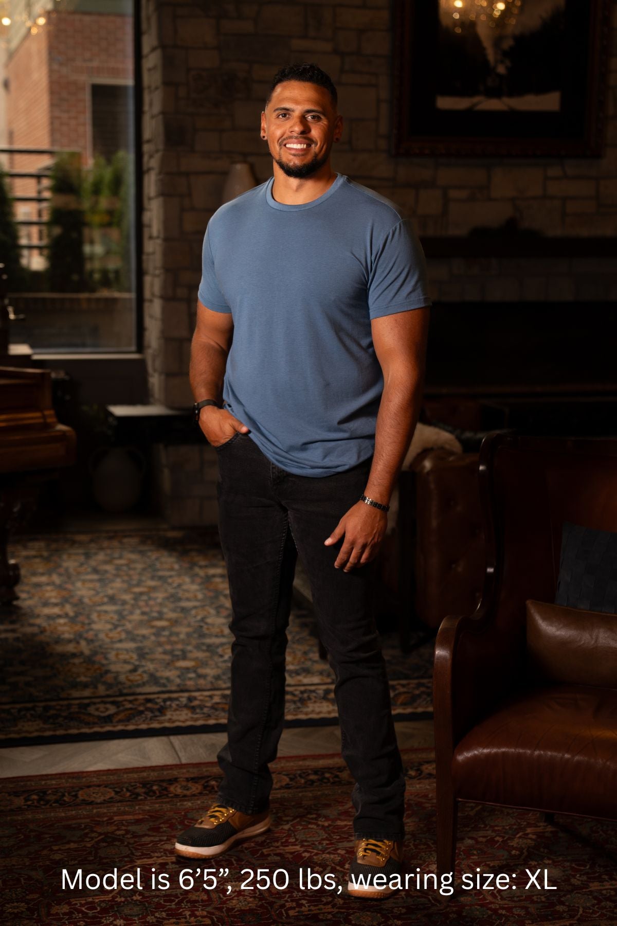 6'5", 250 pound man wearing a blue XL t-shirt and dark pants standing in a room with a fireplace and leather chair.